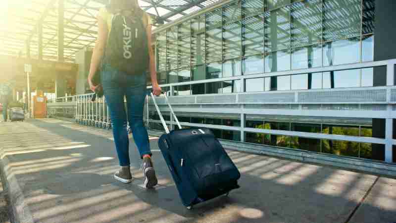 A woman walks with a suitcase outside an airport terminal, ready for travel., tags: reisetipps - pexel