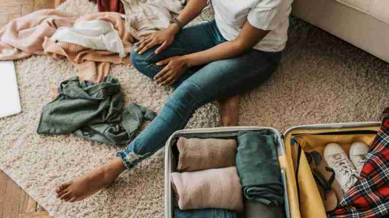 Woman organizing clothes while sitting on floor with open suitcase, preparing for a trip., tags: und - pexel
