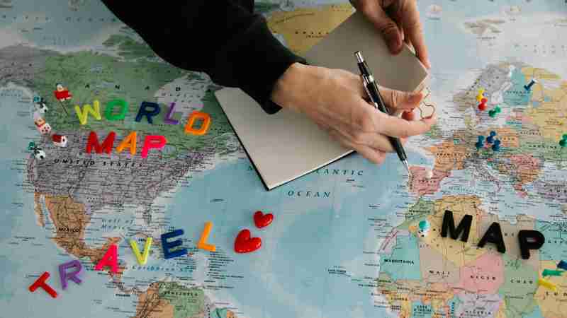 Hands holding pen and notebook over vibrant world map planning a journey., tags: nachhaltiges - pexel